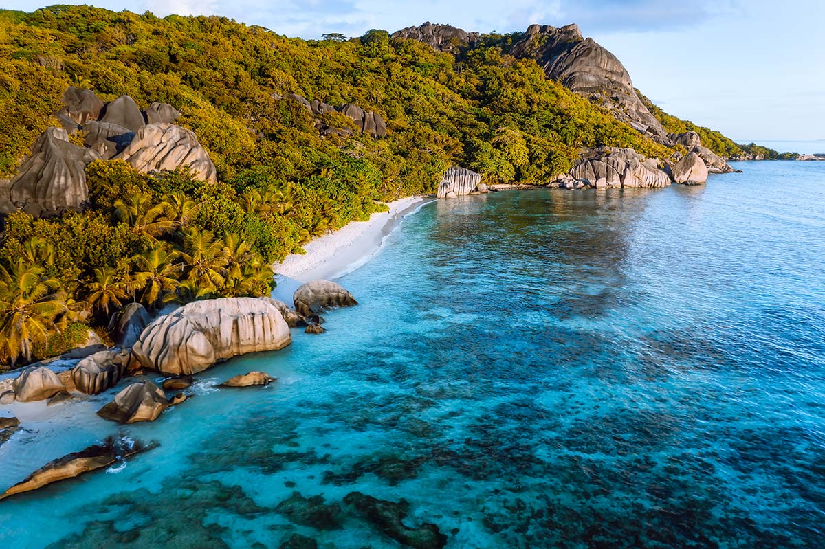 Exotic coastal beach at golden hour — warm amber light, calm turquoise water, tropical setting, bright airy atmosphere